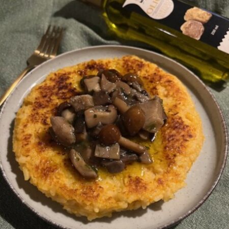Riso al salto dorato con funghi trifolati e bottiglia di olio al tartufo bianco sullo sfondo.
