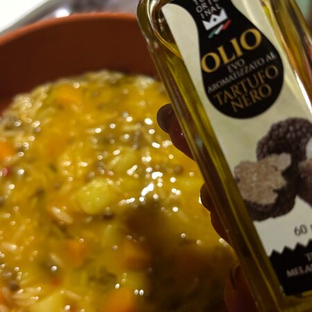 Minestra di verdure con lenticchie, zucca e patate, in primo piano una bottiglia da 60 ml di olio al tartufo nero Tube Original.