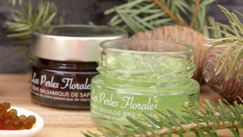 Due vasetti di Les Perles Florales, all’aceto balsamico di abete e al rosmarino selvatico, su sfondo di rami di abete