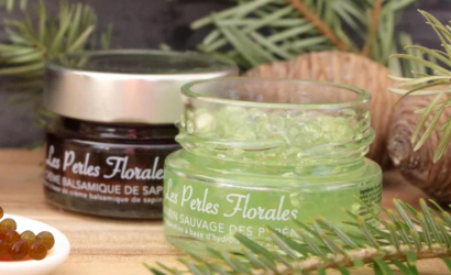 Due vasetti di Les Perles Florales, all’aceto balsamico di abete e al rosmarino selvatico, su sfondo di rami di abete