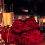 Tavola apparecchiata per una cena romantica con calici di bollicine, rose rosse e candele accese.