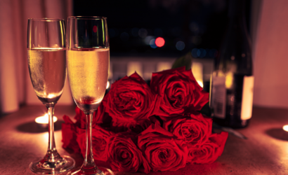 Tavola apparecchiata per una cena romantica con calici di bollicine, rose rosse e candele accese.
