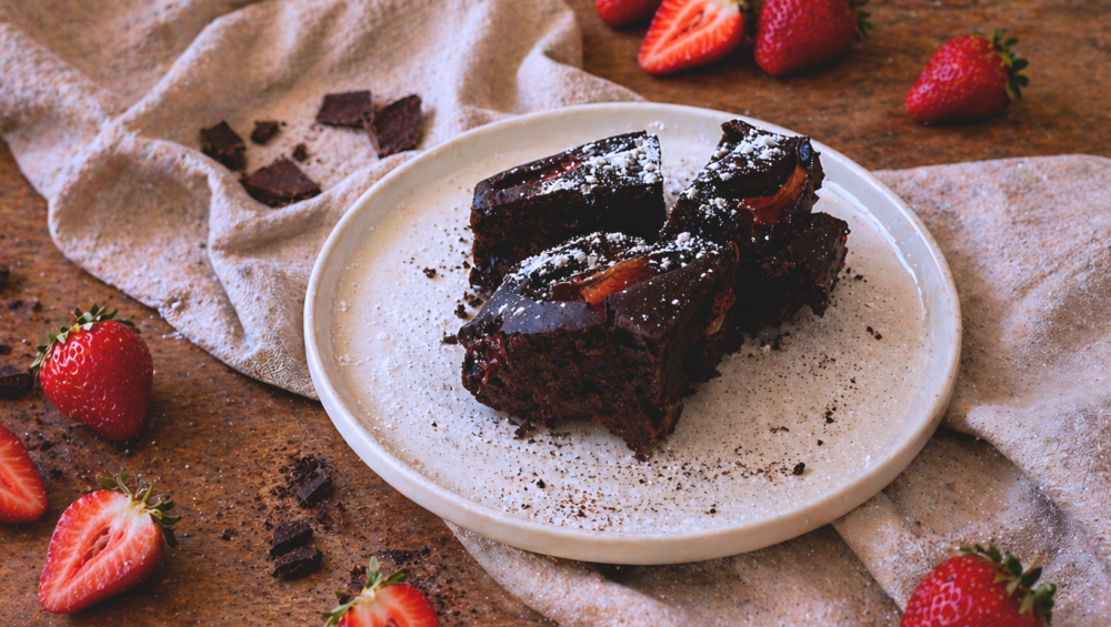 Brownies al cioccolato fondente con fragole fresche e polvere di aglio nero su piatto rustico