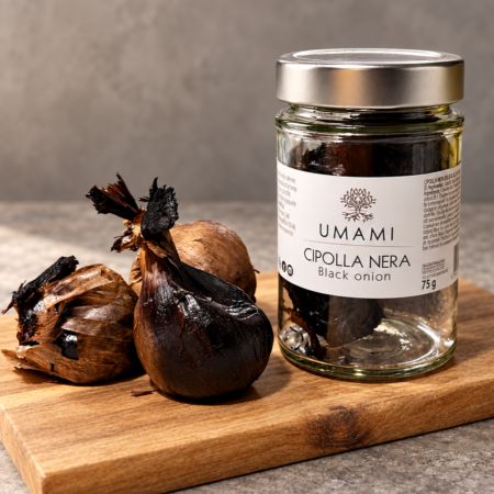 Vasetto di Cipolla Nera UMAMI da 75 g accanto a cipolle nere intere, su un tagliere di legno