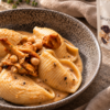 Conchiglioni con crema di ceci e finferli in un piatto fondo, accanto alla confezione di aglio nero a spicchi UMAMI.